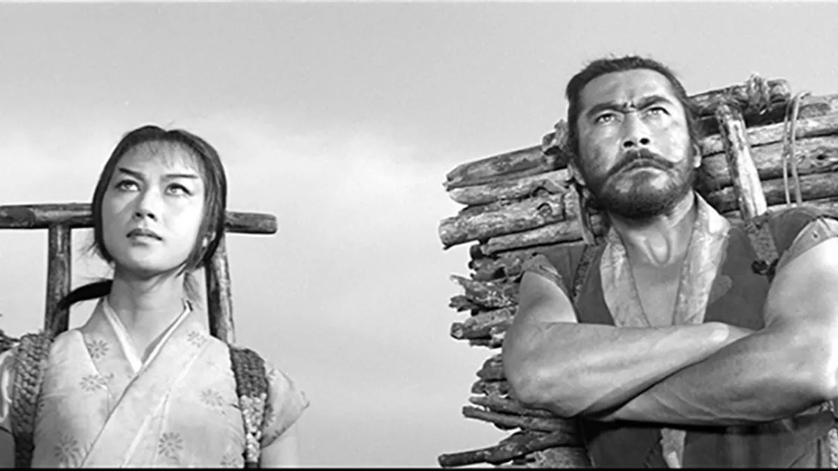 Two figures carrying a load of firewood on their backs, a delivery on the move, in a scene from Akira Kurosawa's The Hidden Fortress (1958)