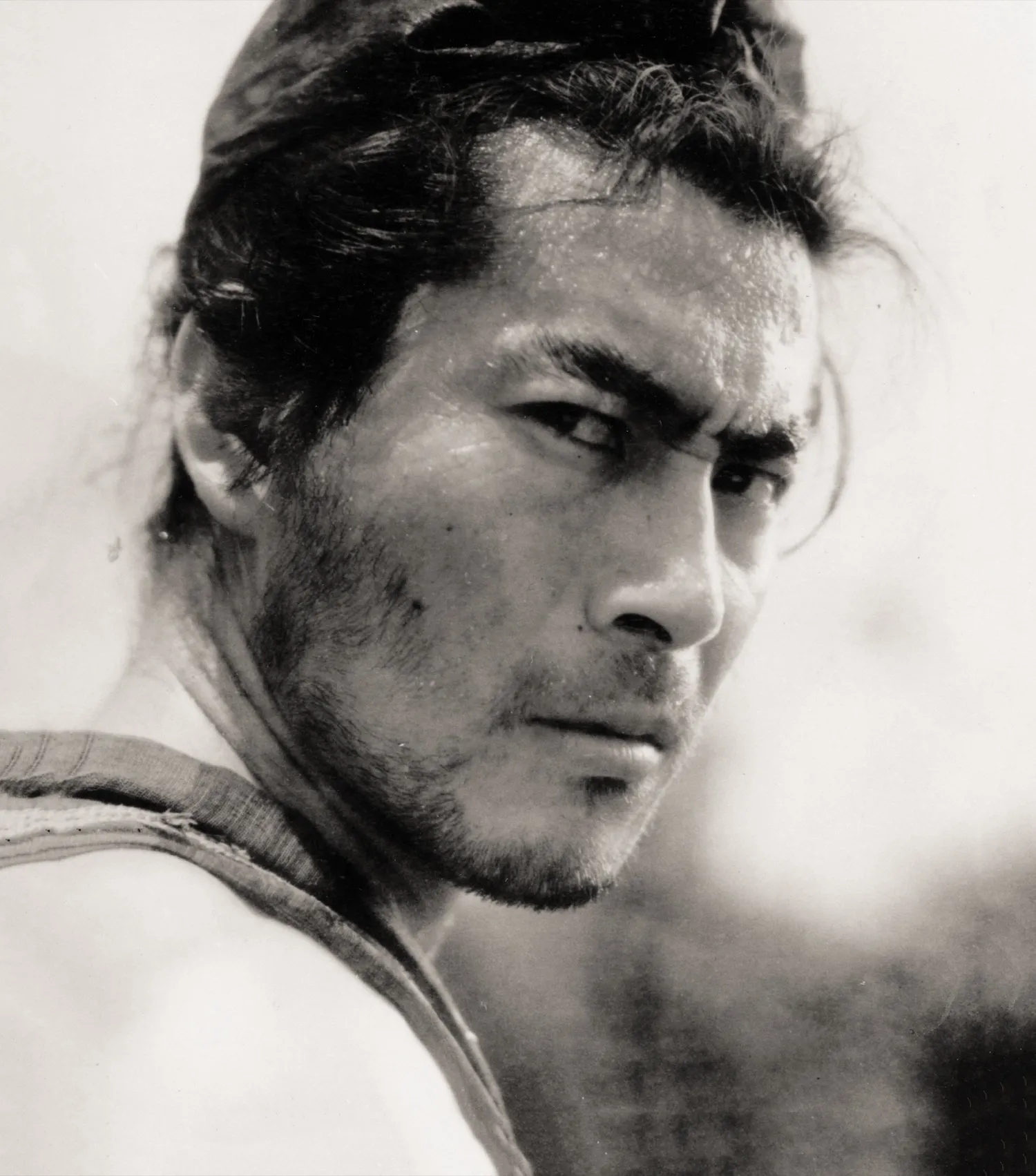 Toshiro Mifune as a samurai, looking back over his shoulder with an intense, watchful expression, in black and white