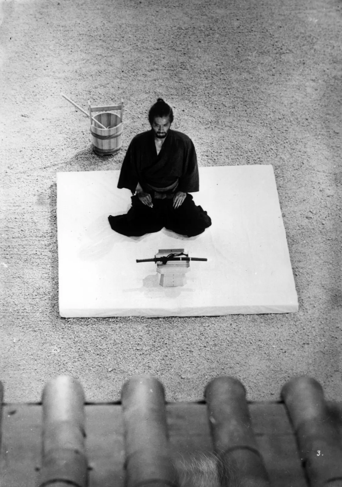 An overhead view of a lone figure kneeling before a sword on a stand, a moment of reckoning, in a scene from Masaki Kobayashi's Harakiri (1962)