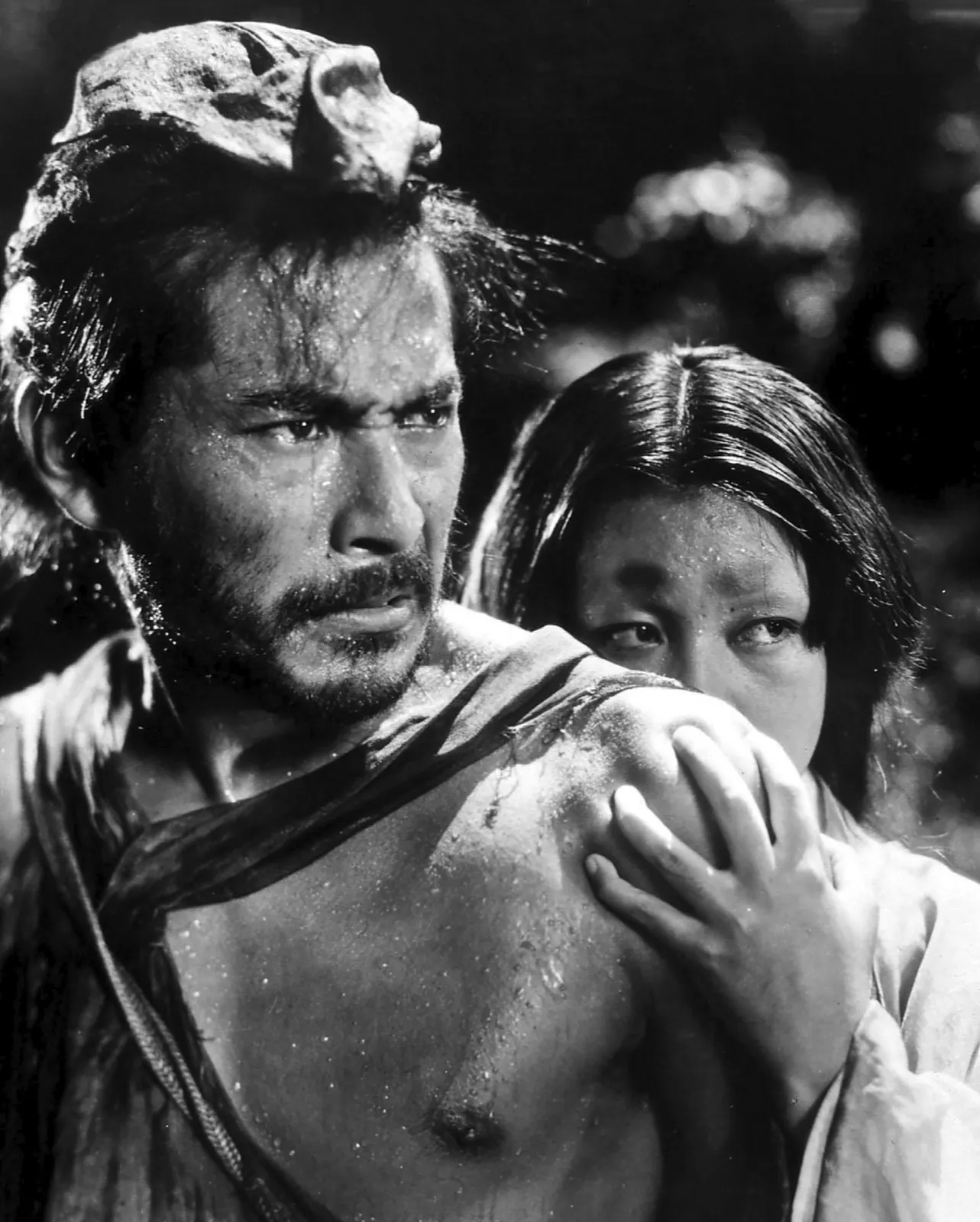 A drenched samurai shielding a young woman in the rain, a close and tense two-shot, in a scene from Akira Kurosawa's Rashomon (1950)