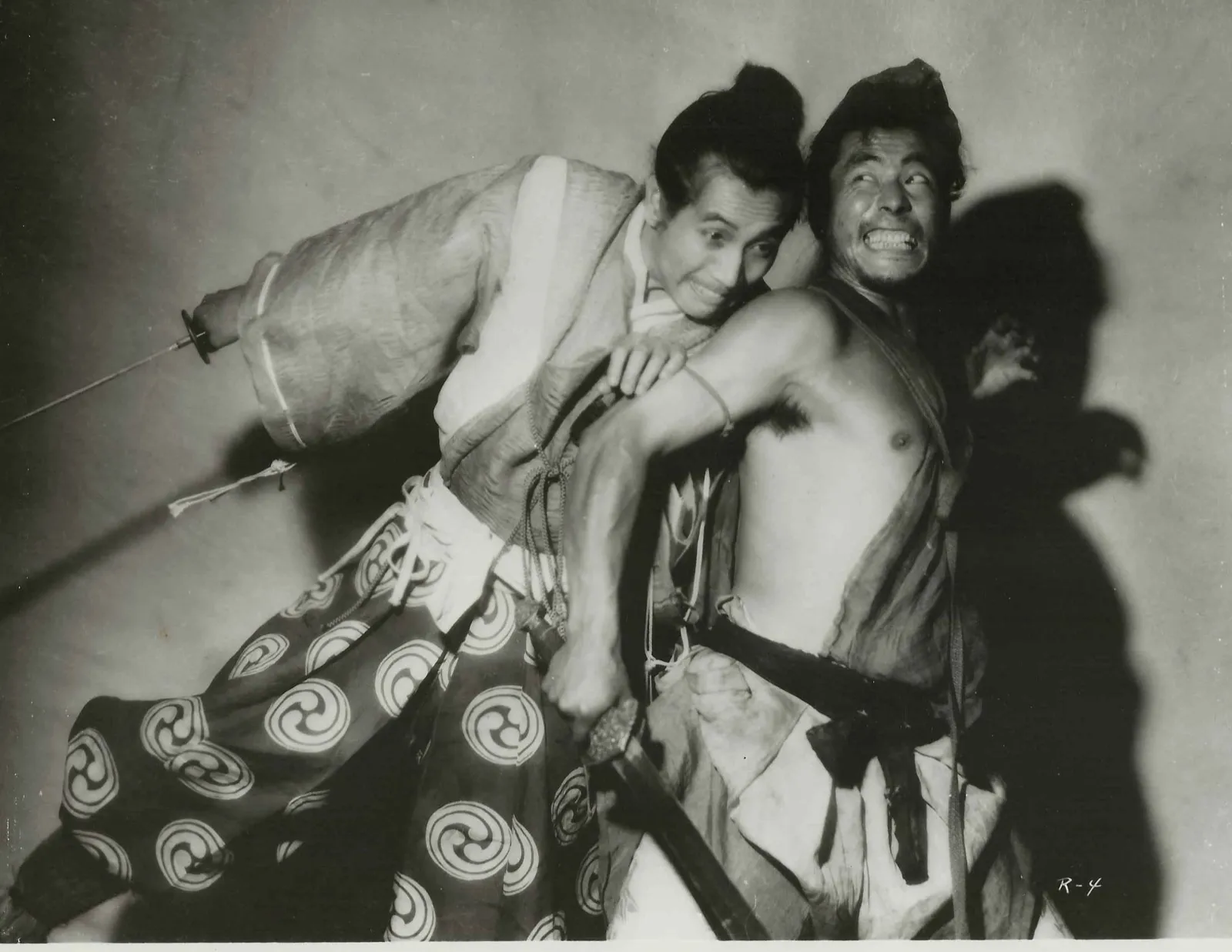 Two men locked together in a violent struggle, a samurai in pale robes and a ragged bandit, each the source of a different account of the same event, in a scene from Akira Kurosawa's Rashomon (1950)