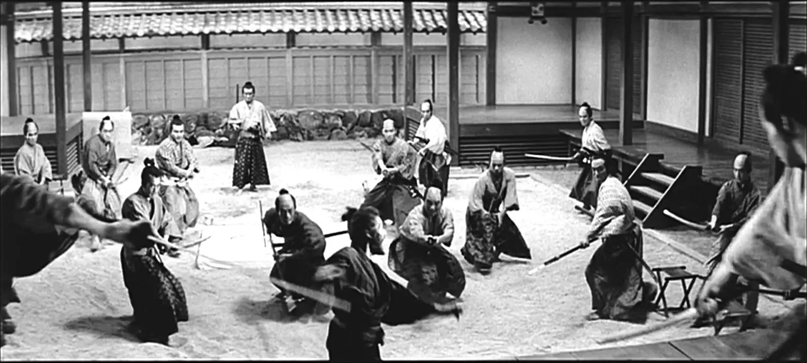 A single figure standing amid a ring of many samurai in a sand courtyard, in a scene from Akira Kurosawa's Sanjuro (1962)