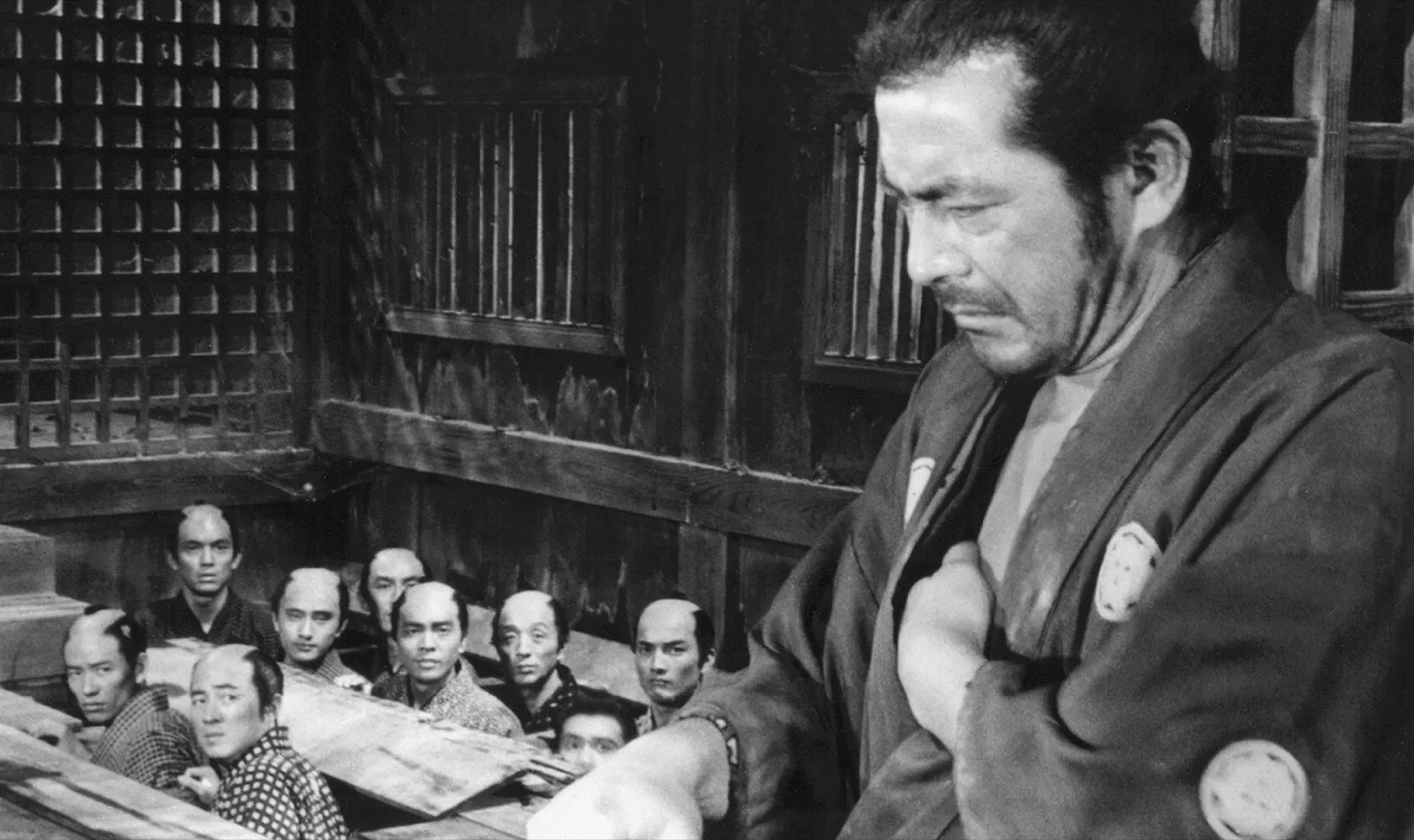 An experienced ronin stands in the foreground, unimpressed, while a group of young samurai gather below and look up to him, from Akira Kurosawa's Sanjuro (1962)