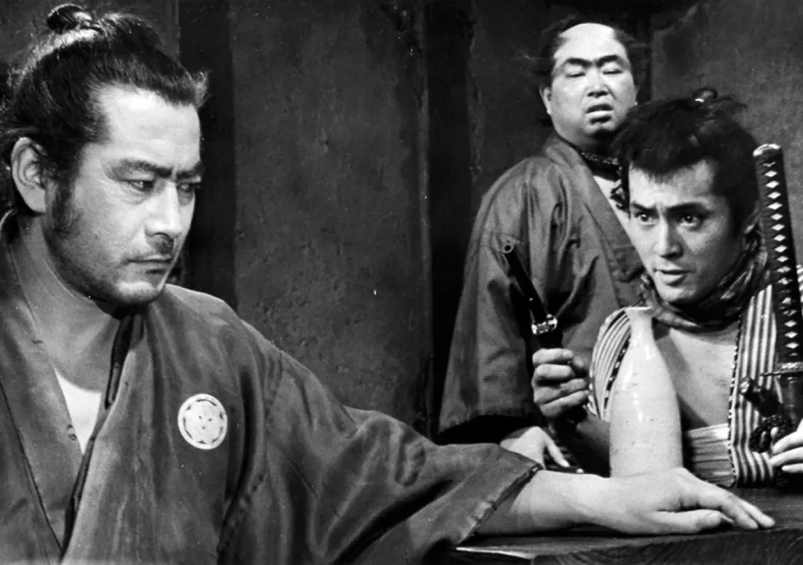 The ronin sizing up a room while others watch behind him, in a scene from Akira Kurosawa's Yojimbo (1961)
