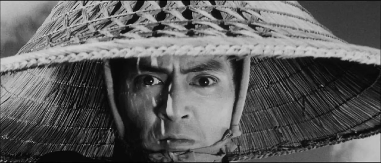 An extreme close-up of a swordsman's intense eyes reading the moment from beneath a woven straw hat