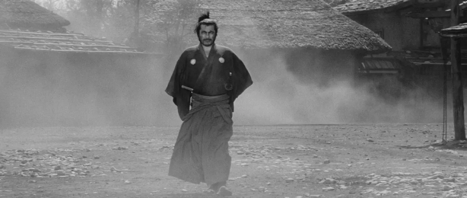 A lone samurai walking forward through drifting dust in a deserted town, resolute, in black and white